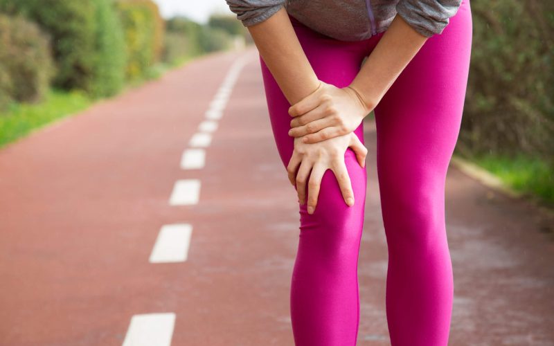Female jogger wearing pink tights, injuring knee. Closeup of female hand holding leg. Athletic injury concept
